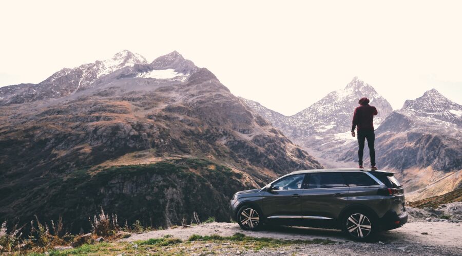 man standing on black 5-door hatchback across brown glacier mountains