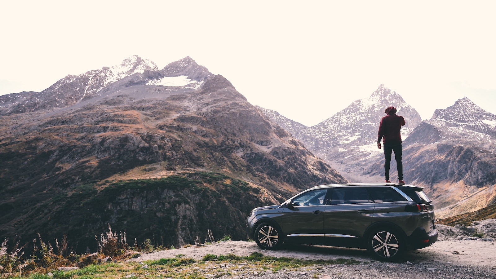 man standing on black 5-door hatchback across brown glacier mountains